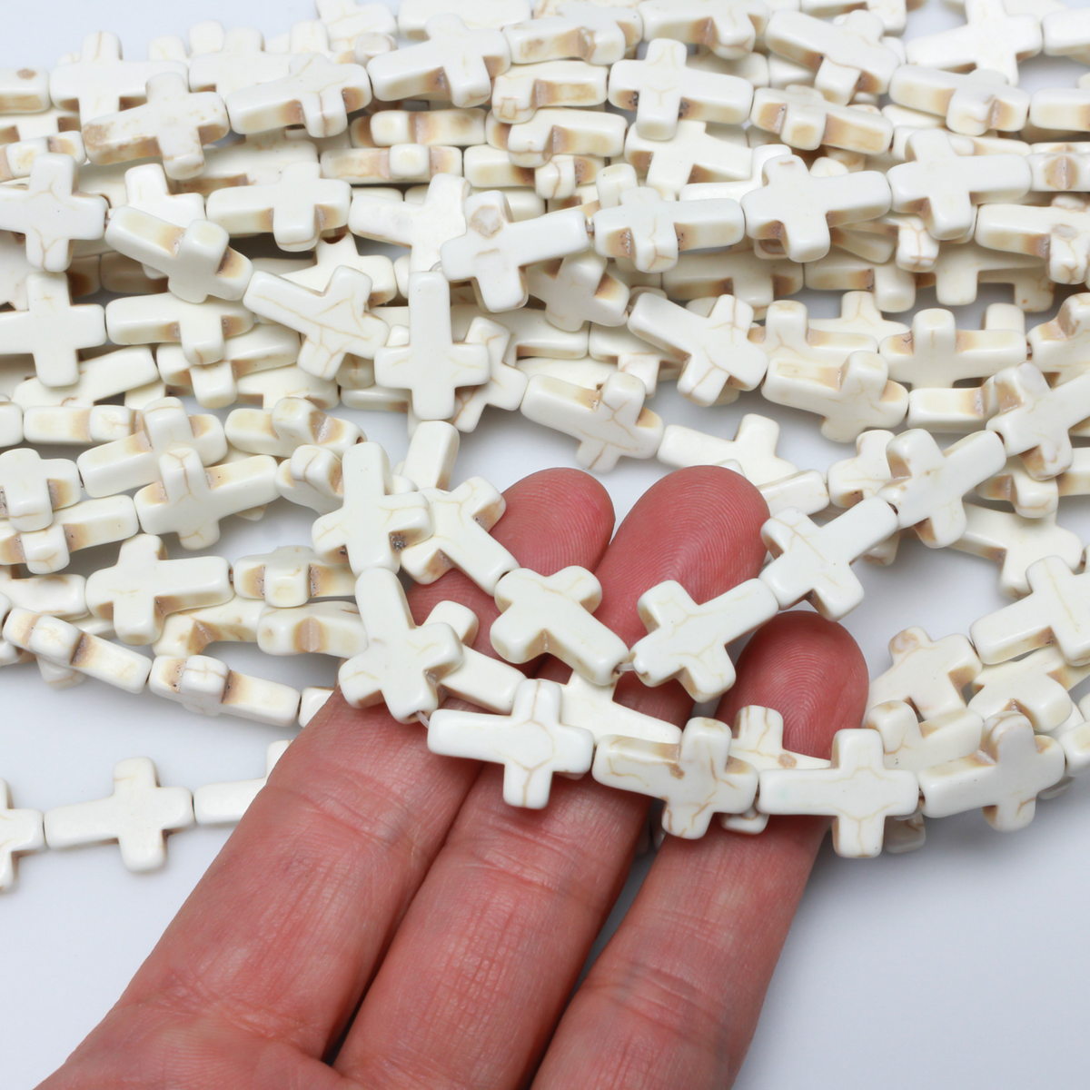 Beige cross shaped beads that are a synthetic turquoise material dyed an off-white beige color. Sold by the strand