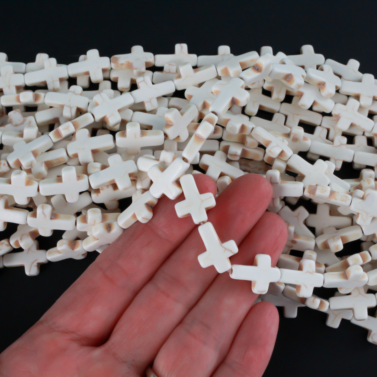 Beige cross shaped beads that are a synthetic turquoise material dyed an off-white beige color. Sold by the strand