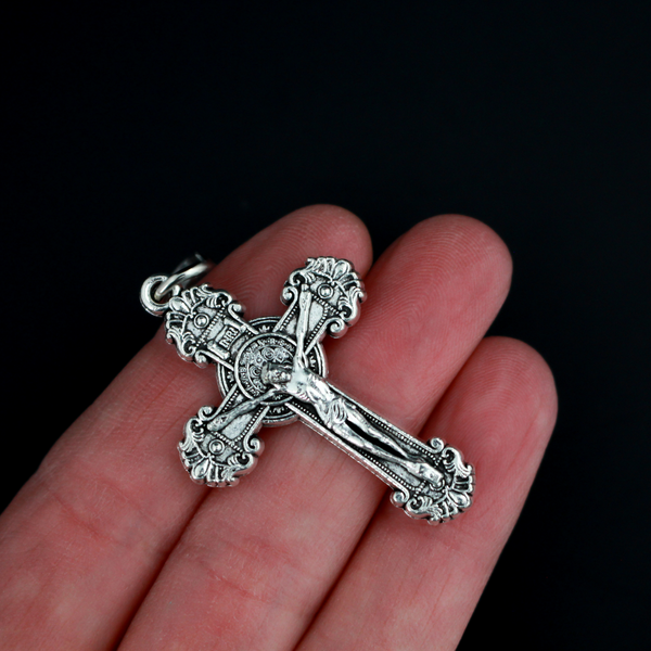 ornate crucifix crosses in an antiqued silver-tone color with the medal of Saint Benedict behind Jesus