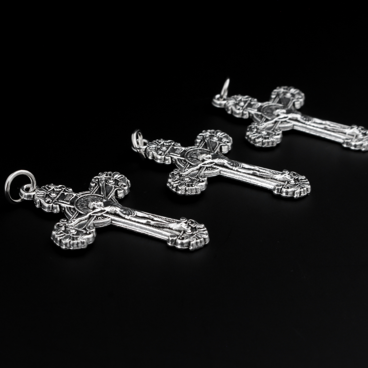 ornate crucifix crosses in an antiqued silver-tone color with the medal of Saint Benedict behind Jesus