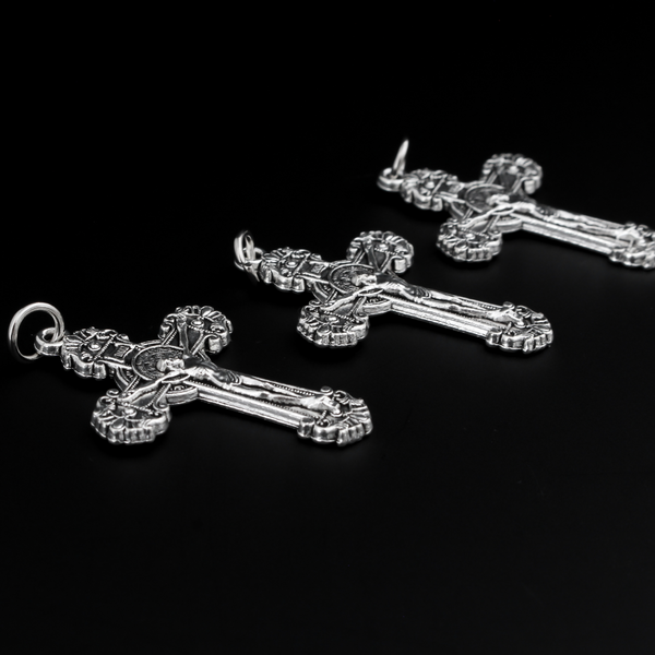 ornate crucifix crosses in an antiqued silver-tone color with the medal of Saint Benedict behind Jesus