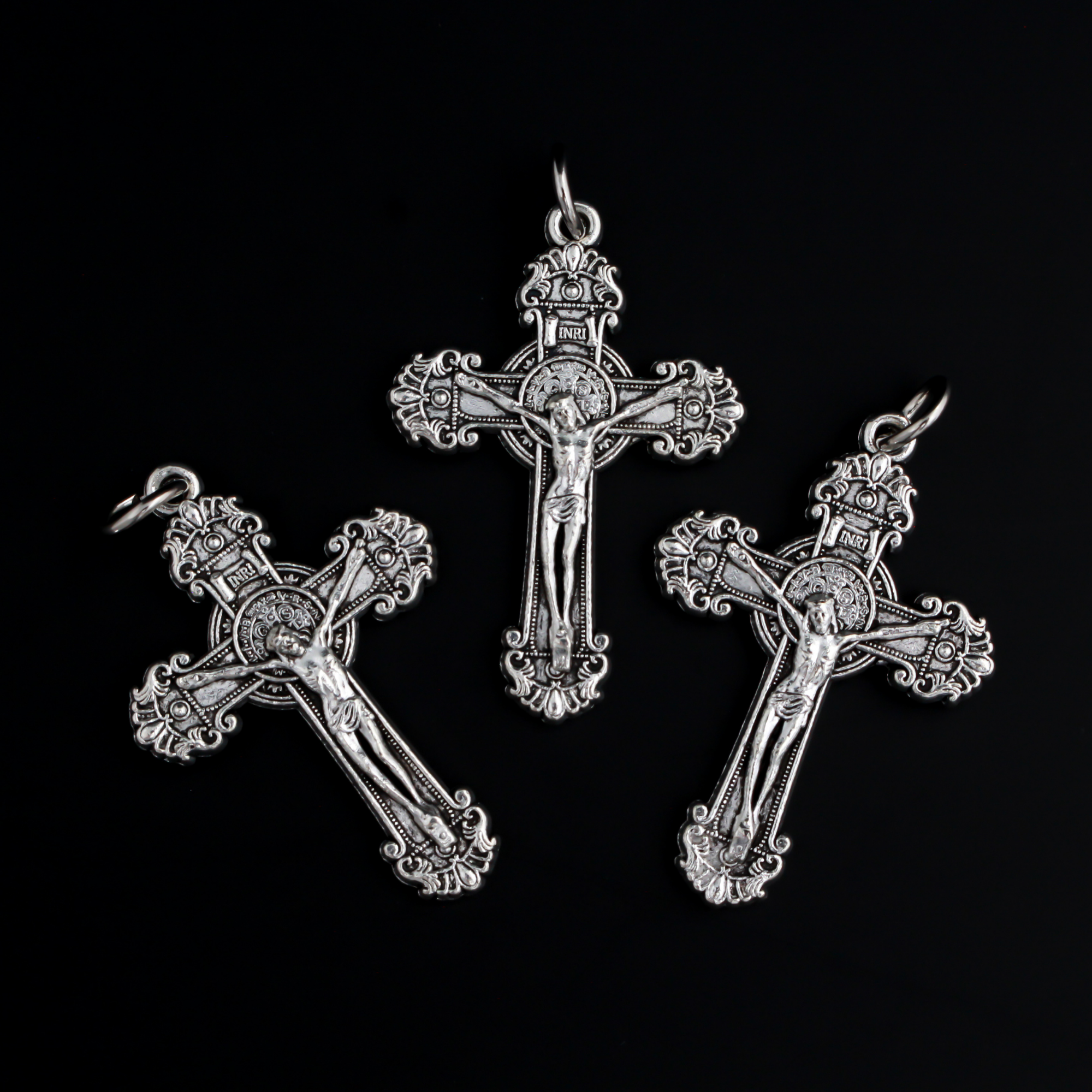 ornate crucifix crosses in an antiqued silver-tone color with the medal of Saint Benedict behind Jesus