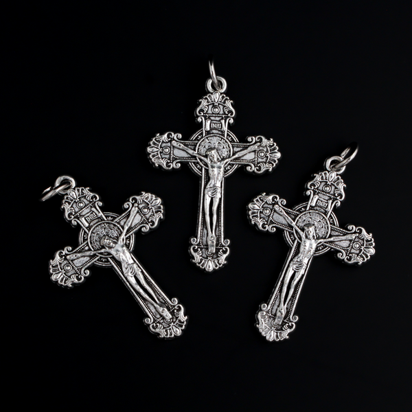 ornate crucifix crosses in an antiqued silver-tone color with the medal of Saint Benedict behind Jesus