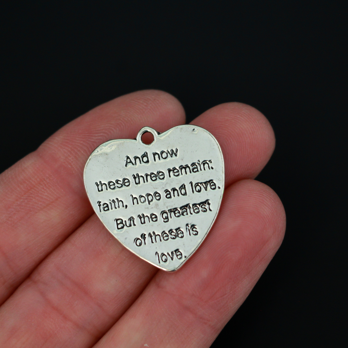 Shiny silver heart charms engraved with a bible passage from First Corinthians 13:13 “And now these three remain: faith, hope and love. But the greatest of these is love." The backside of the charm is blank with a pattern.