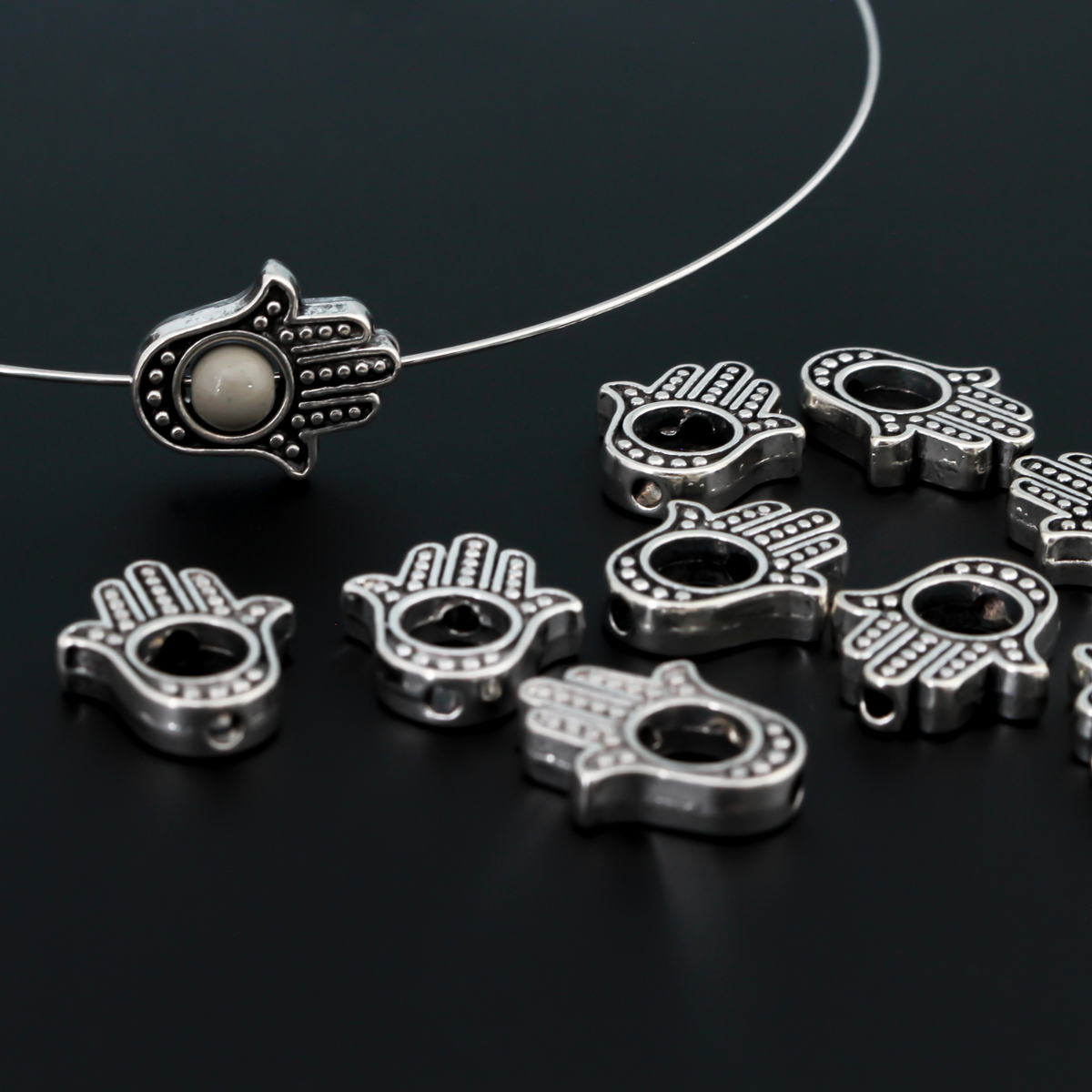 Hamsa hand bead frame crafted of zinc alloy and plated with an antiqued silver finish, it features a raised dot pattern on both sides and fits a 4mm round bead or smaller