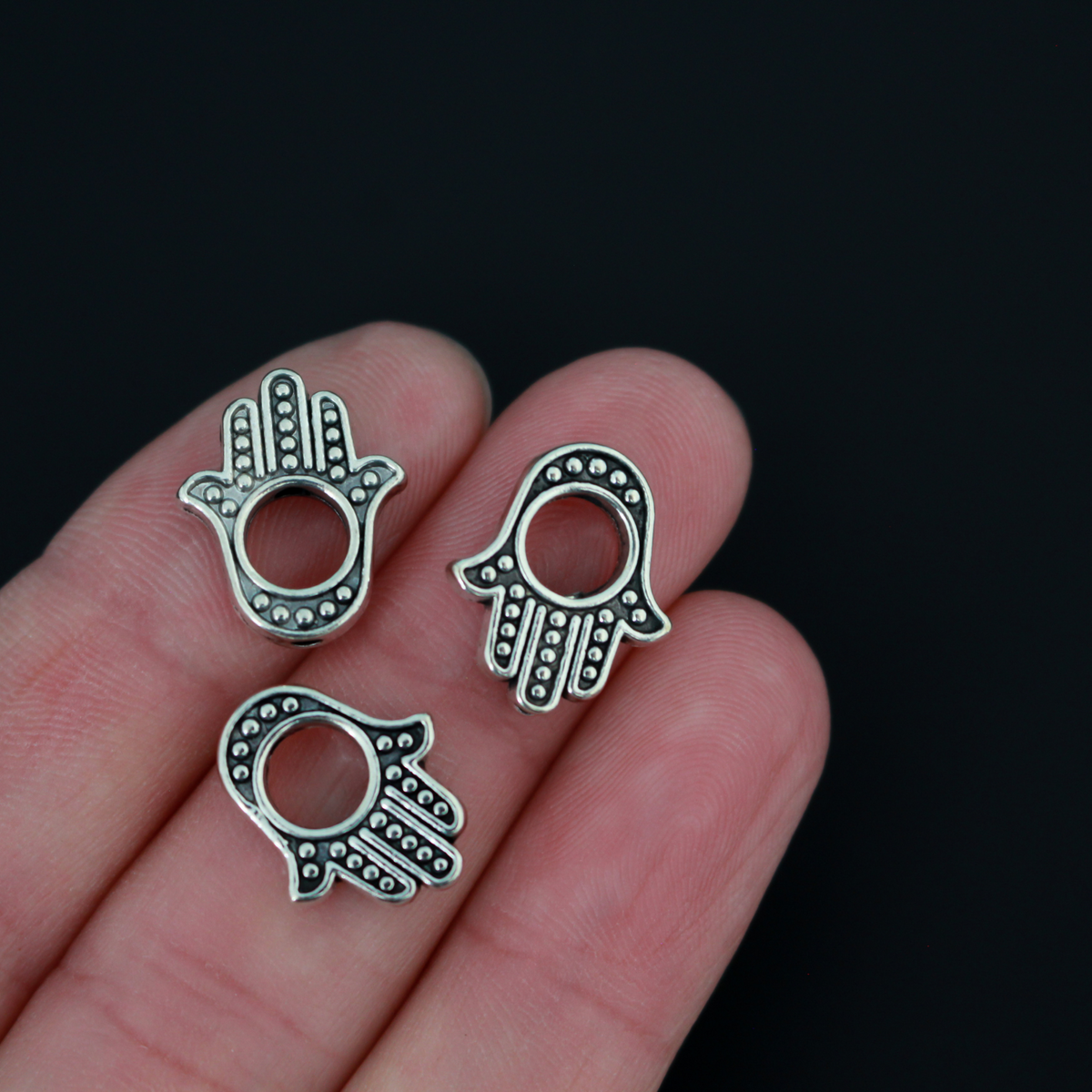 Hamsa hand bead frame crafted of zinc alloy and plated with an antiqued silver finish, it features a raised dot pattern on both sides and fits a 4mm round bead or smaller