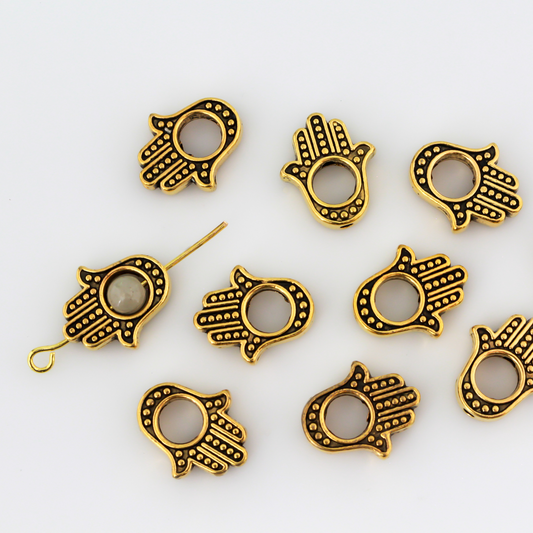 Hamsa hand bead frame crafted from zinc alloy and plated with an antiqued gold finish, it features a raised dot pattern on both sides and fits a 4mm round bead or smaller