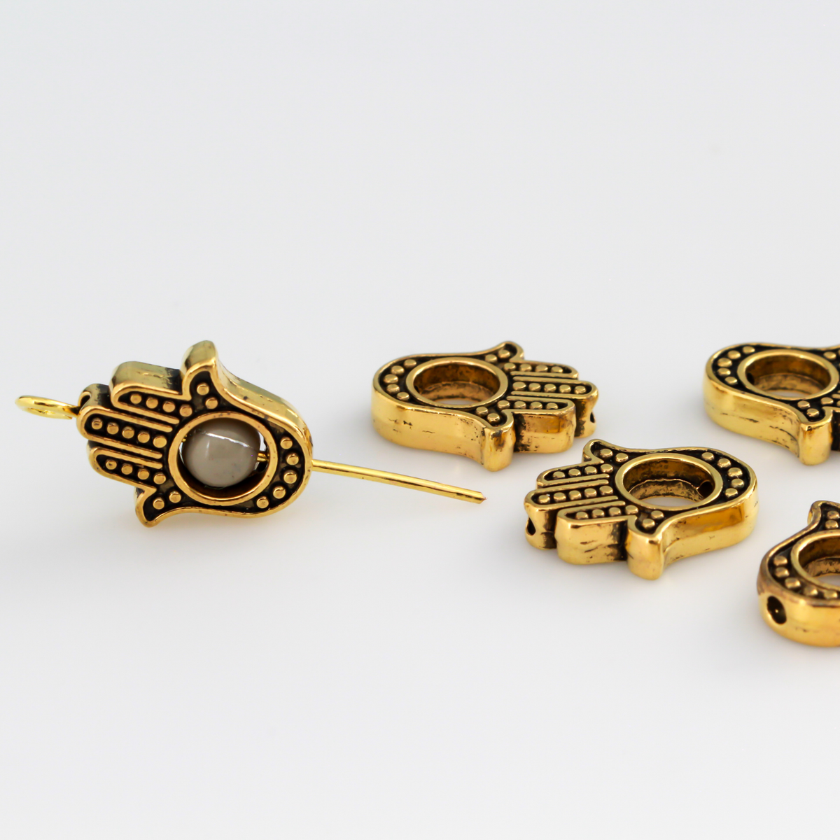 Hamsa hand bead frame crafted from zinc alloy and plated with an antiqued gold finish, it features a raised dot pattern on both sides and fits a 4mm round bead or smaller