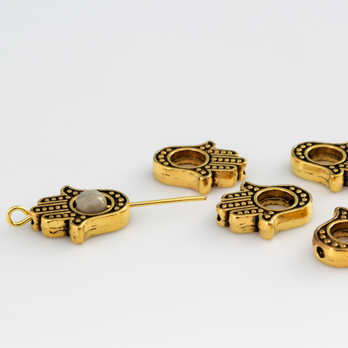 Hamsa hand bead frame crafted from zinc alloy and plated with an antiqued gold finish, it features a raised dot pattern on both sides and fits a 4mm round bead or smaller