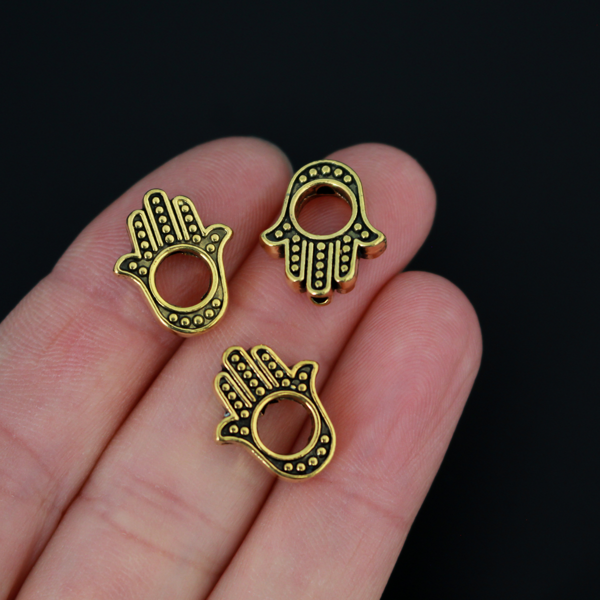 Hamsa hand bead frame crafted from zinc alloy and plated with an antiqued gold finish, it features a raised dot pattern on both sides and fits a 4mm round bead or smaller