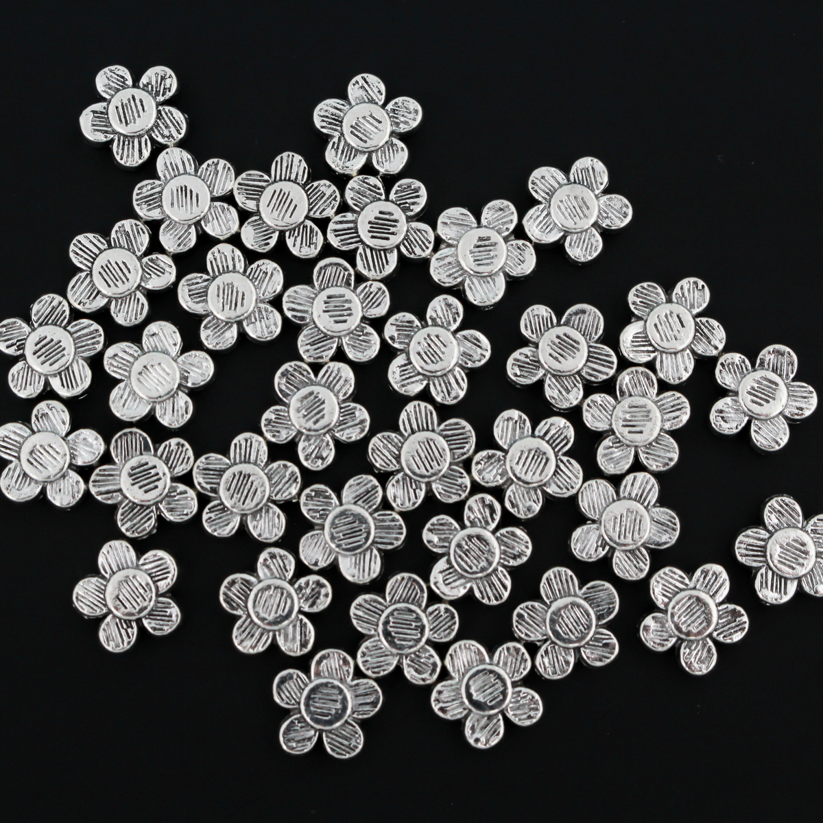 Antiqued silver-tone metal beads that are flat with a raised relief five petal flower pattern on both sides