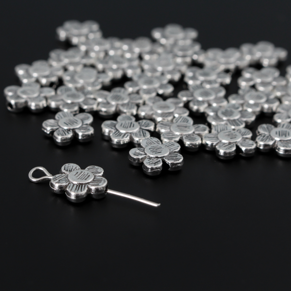 Antiqued silver-tone metal beads that are flat with a raised relief five petal flower pattern on both sides