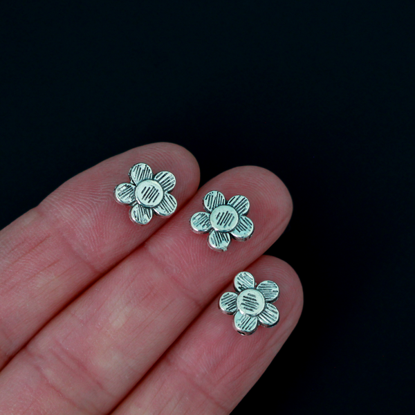 Antiqued silver-tone metal beads that are flat with a raised relief five petal flower pattern on both sides