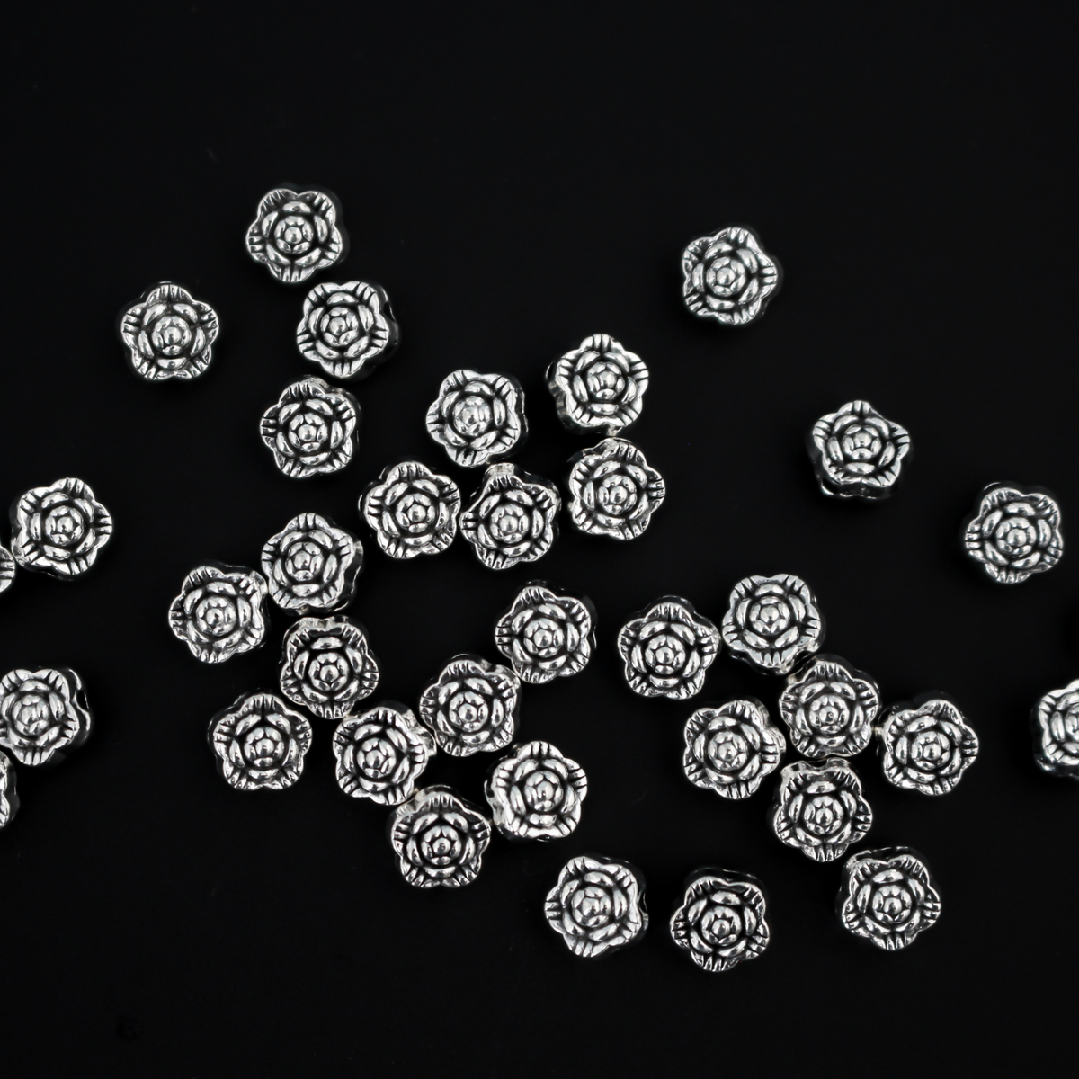 Antiqued silver-tone metal beads that are flat with a raised relief flower pattern on both sides, 6mm diameter by 4mm thick