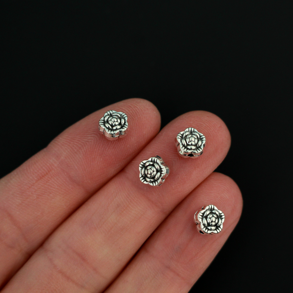 Antiqued silver-tone metal beads that are flat with a raised relief flower pattern on both sides, 6mm diameter by 4mm thick