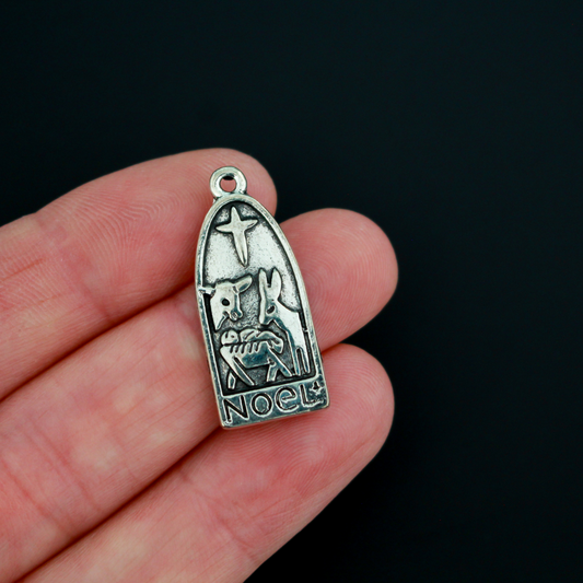 Arched charm depicting Christ child in the manger with the Christmas Star or the Star of Bethlehem above and a donkey and cow on either side