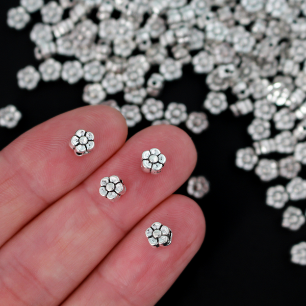 silver-tone metal beads that are flat with a raised relief five petal flower pattern on both sides