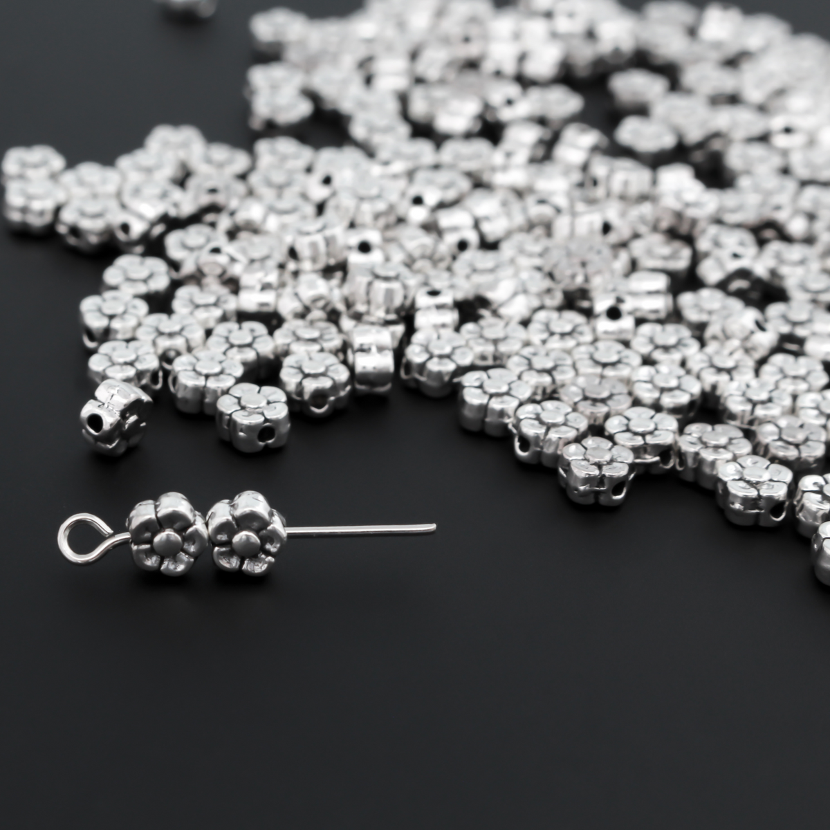 silver-tone metal beads that are flat with a raised relief five petal flower pattern on both sides