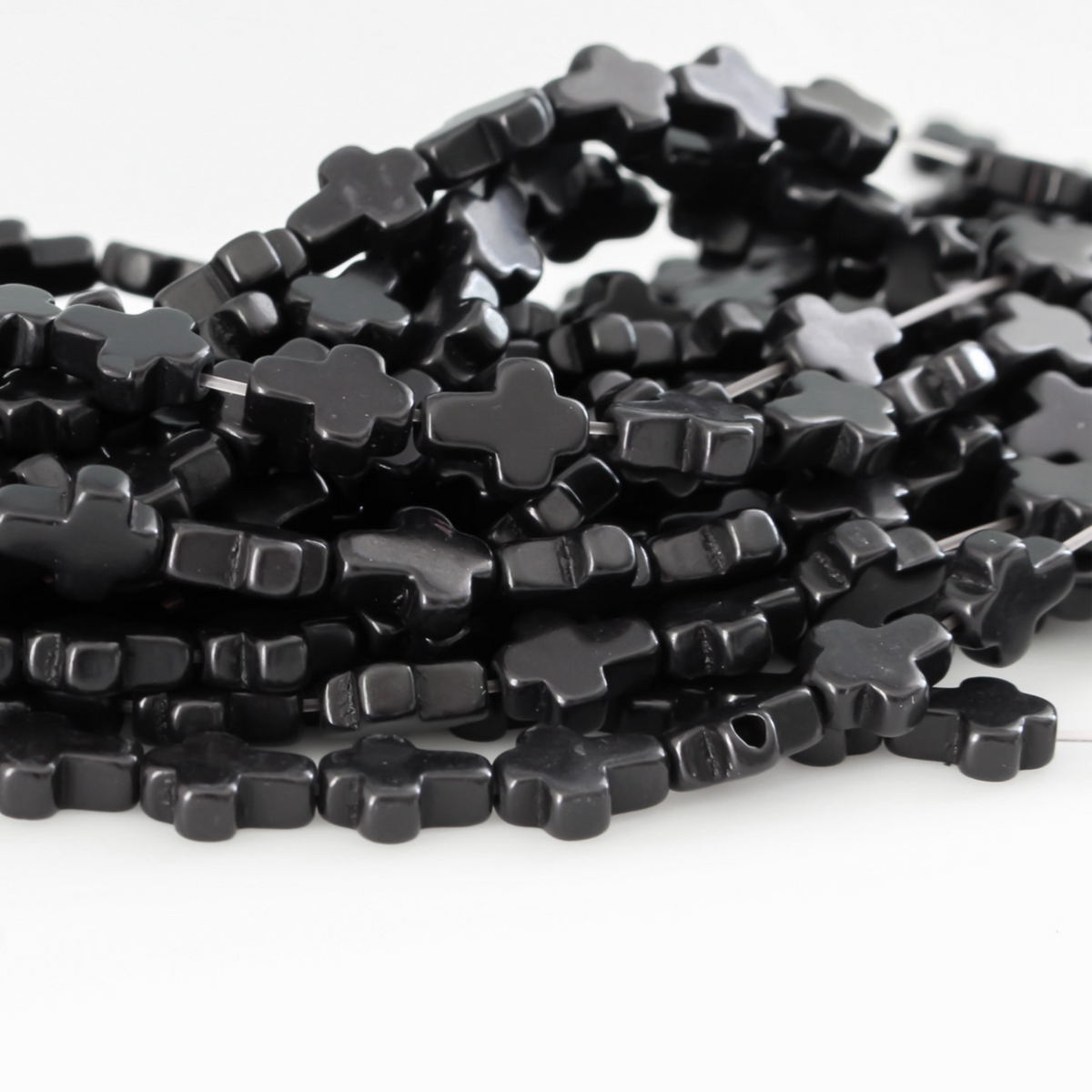 Black cross shaped beads that are a synthetic turquoise material dyed black Sold by the strand. Each strand is 16 inches long with about 38pcs/strand.