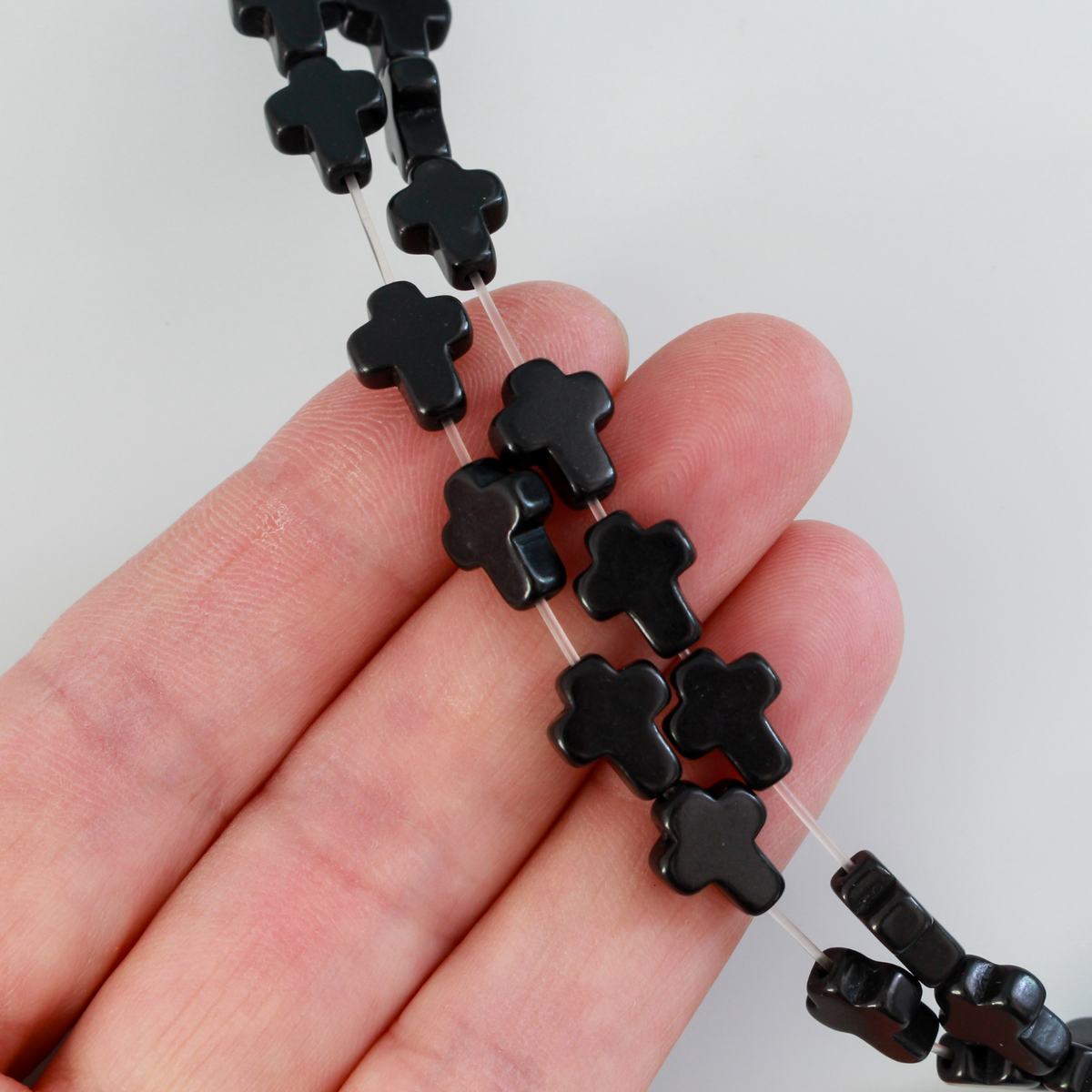 Black cross shaped beads that are a synthetic turquoise material dyed black Sold by the strand. Each strand is 16 inches long with about 38pcs/strand.
