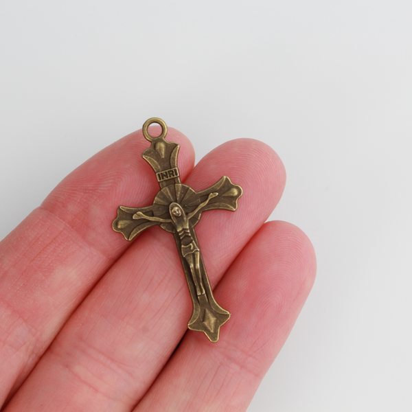 Small crucifix cross in an antiqued bronze color with a starburst design behind Jesus and ornate flared ends