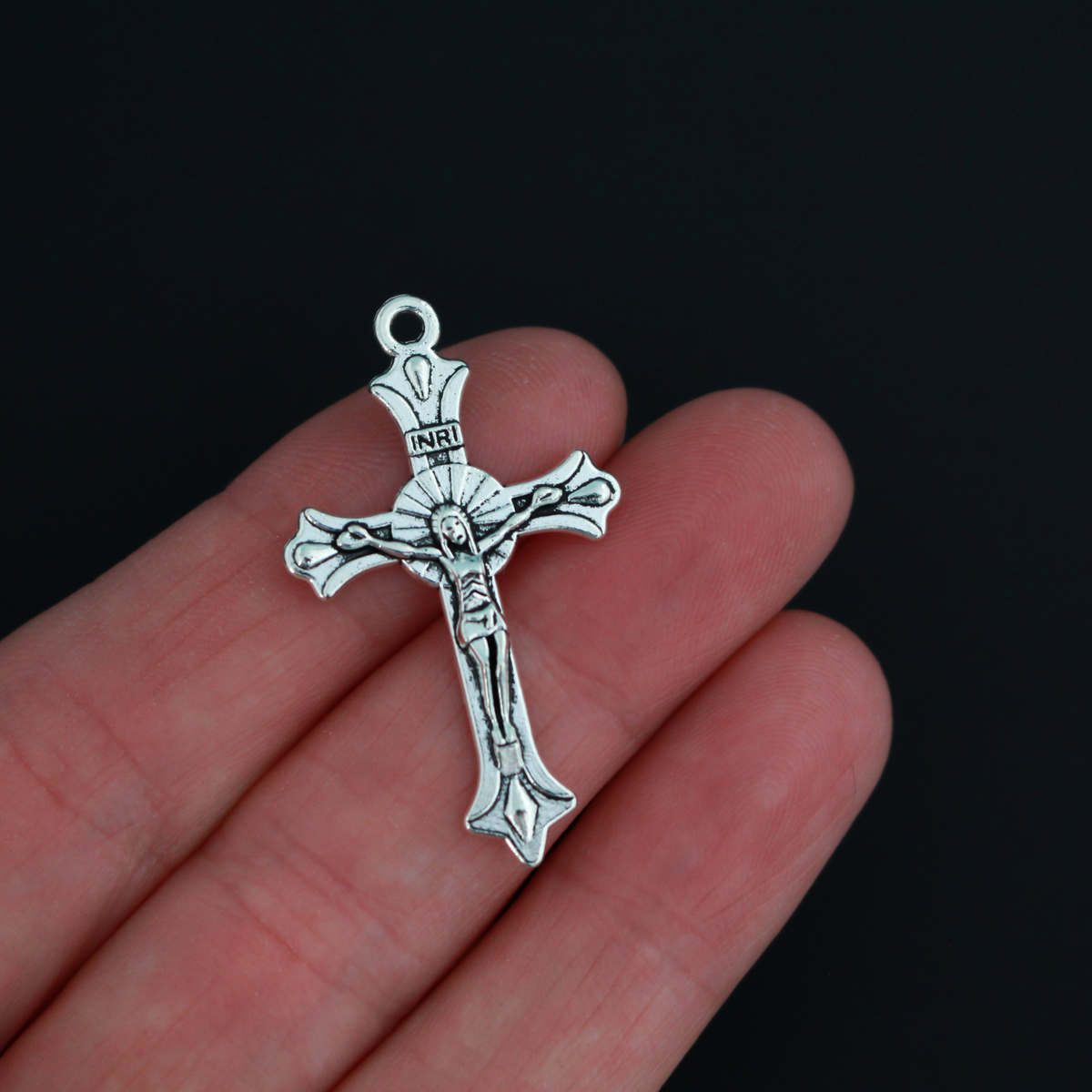 Small crucifix cross in an antiqued silver color with a starburst design behind Jesus and ornate flared ends.
