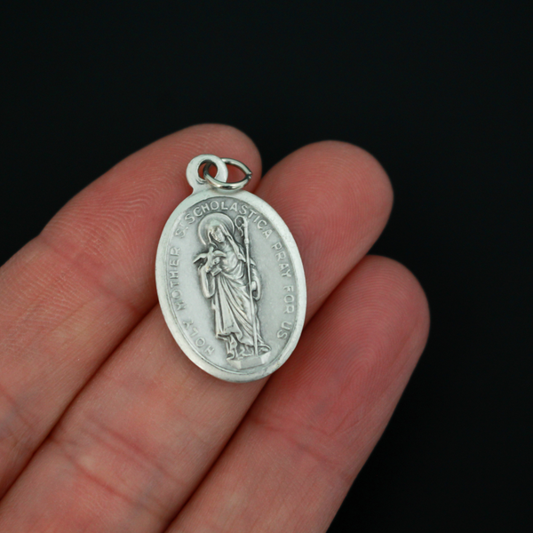 Holy Mother Saint Scholastica medal that depicts the saint on the front and is marked "Pray For Us" on the back