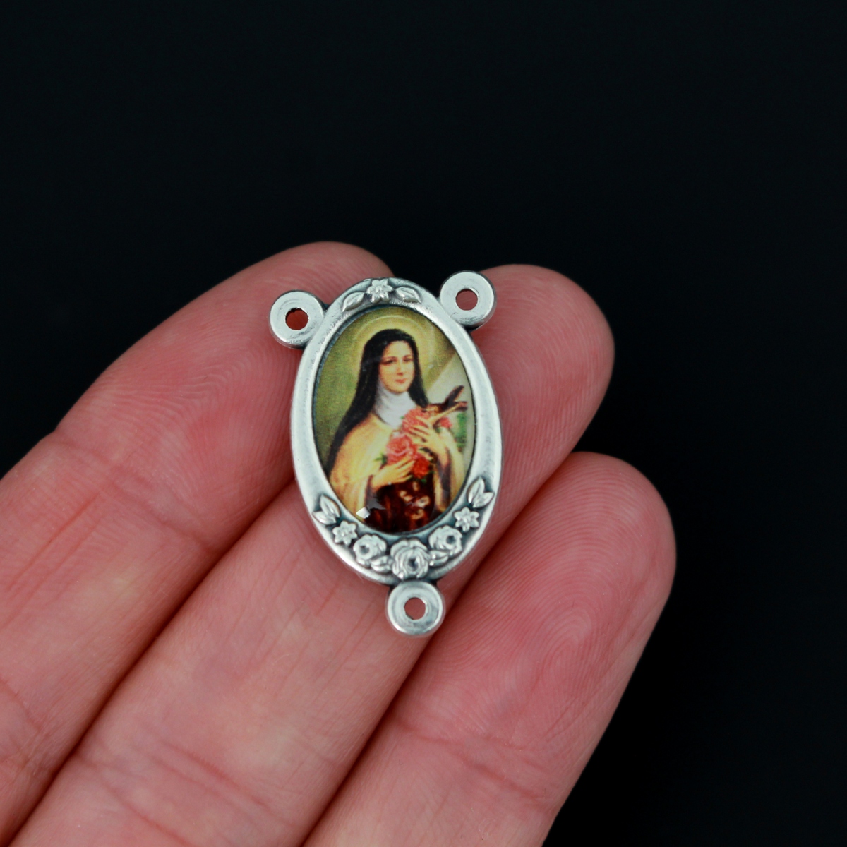 Rosary center that has a color image of Saint Therese of Lisieux inlaid in a silver oxidized Center with a flower detail on the edge
