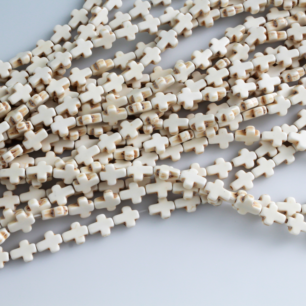 Beige cross shaped beads that are a synthetic turquoise material that is dyed an off-white beige color with a rustic look