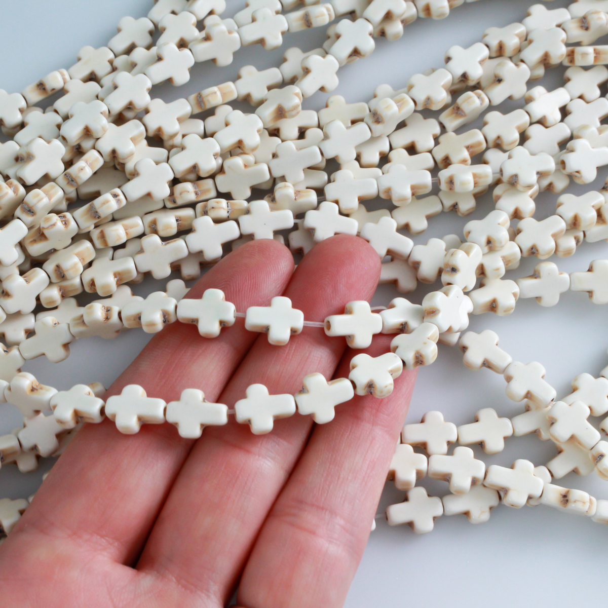 Beige cross shaped beads that are a synthetic turquoise material that is dyed an off-white beige color with a rustic look