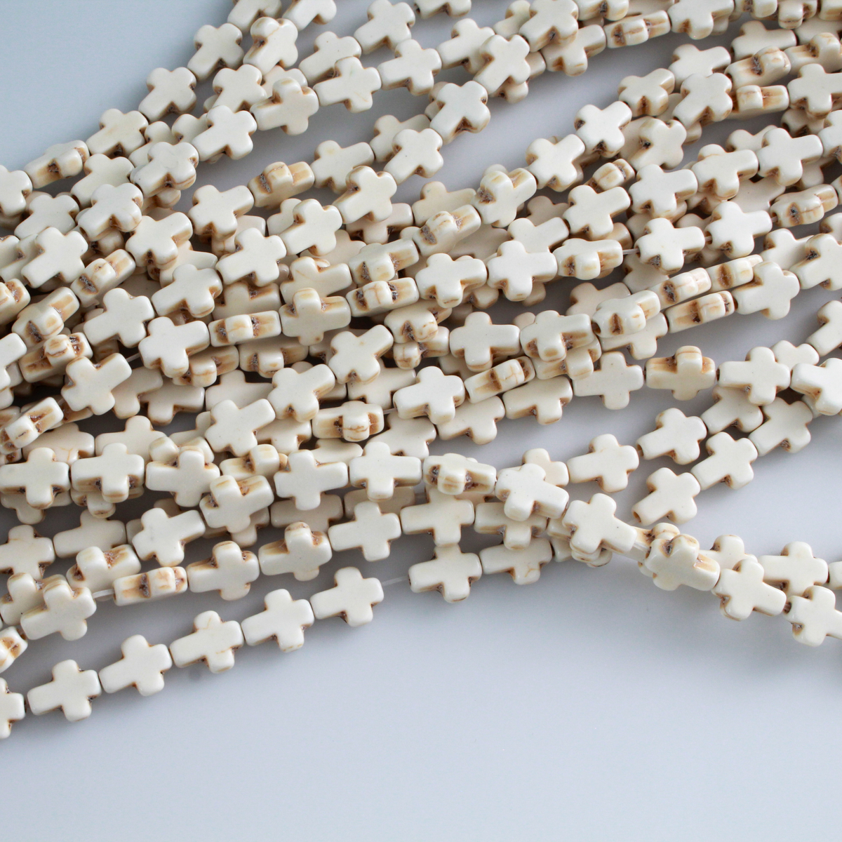 Beige cross shaped beads that are a synthetic turquoise material that is dyed an off-white beige color with a rustic look