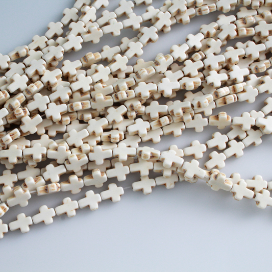 Beige cross shaped beads that are a synthetic turquoise material that is dyed an off-white beige color with a rustic look