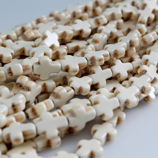 Beige cross shaped beads that are a synthetic turquoise material that is dyed an off-white beige color with a rustic look