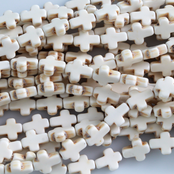 Beige cross shaped beads that are a synthetic turquoise material that is dyed an off-white beige color with a rustic look
