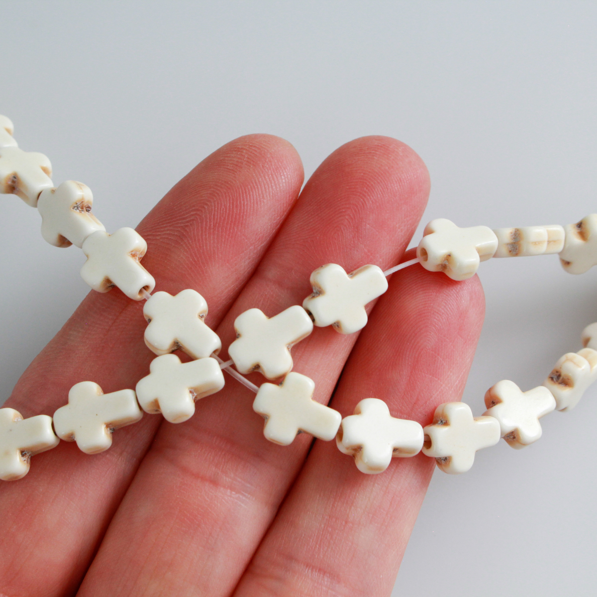 Beige cross shaped beads that are a synthetic turquoise material that is dyed an off-white beige color with a rustic look