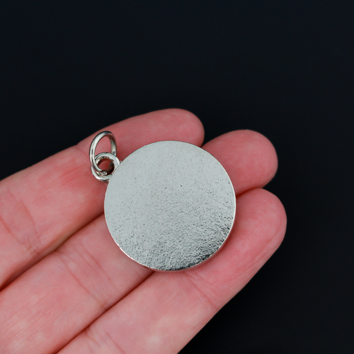 Round pendant with an ornate acronym on the front that is detailed by a light blue enamel color. The acronym ADMG stands for "Ad Majorem Dei Gloriam".