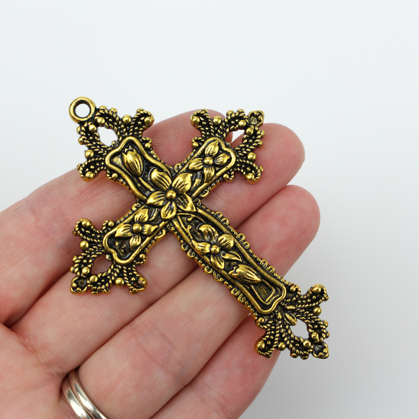 Large ornate cross pendant that has lilies on the crossbars and ornate fleur de lis ends with an antiqued golden color