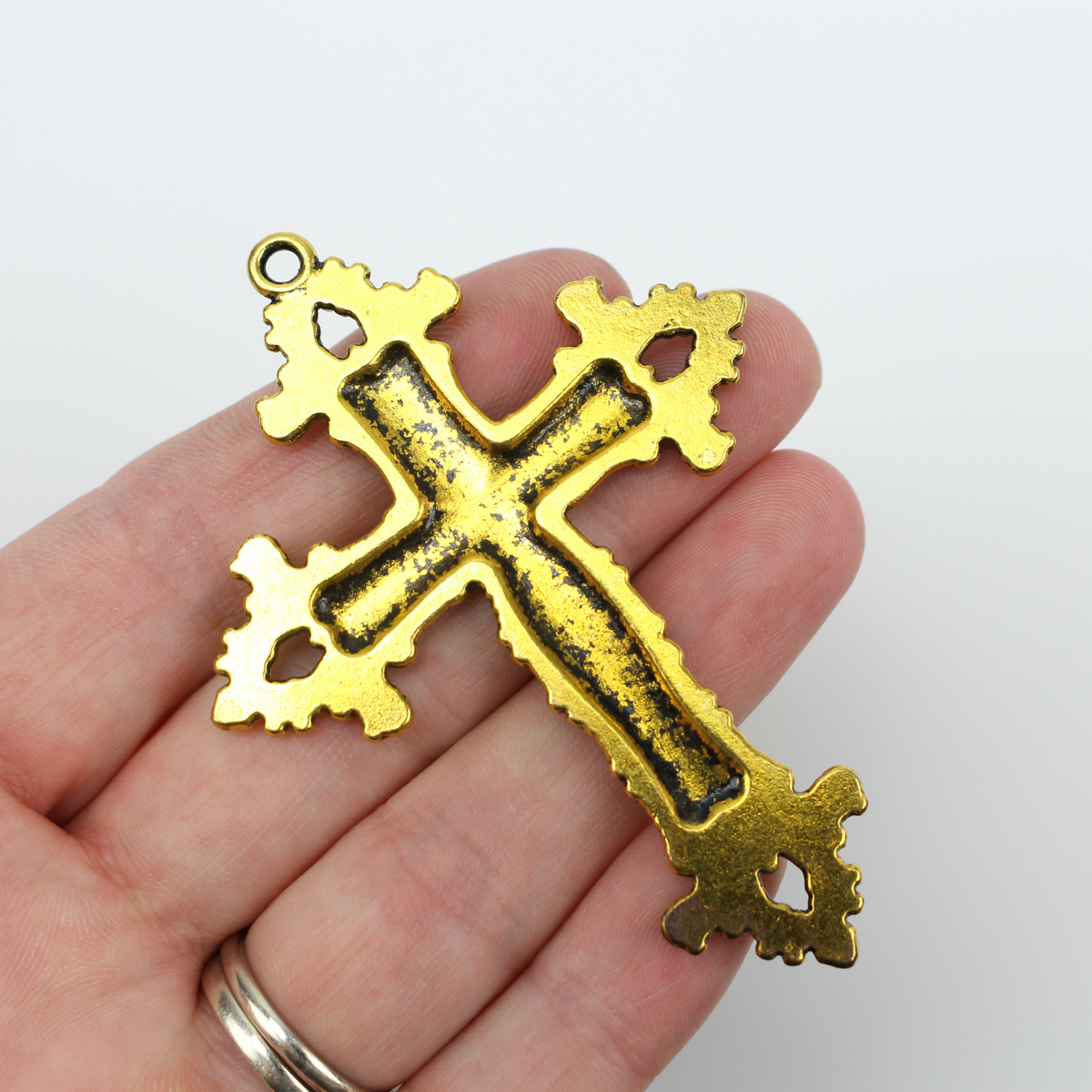 Large ornate cross pendant that has lilies on the crossbars and ornate fleur de lis ends with an antiqued golden color