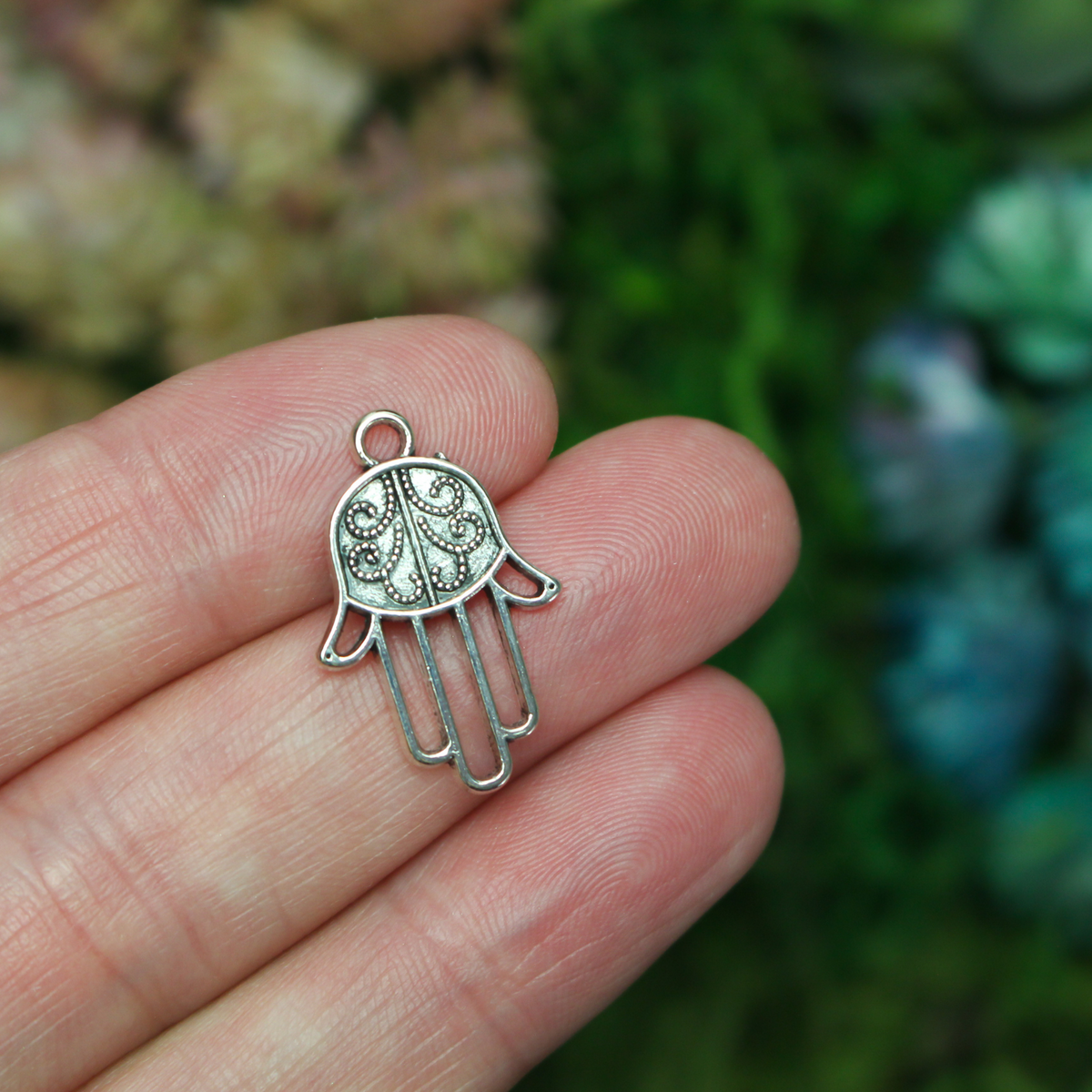 Silver tone Hamsa hand charm with an open design on the fingers, 22mm long by 15mm wide