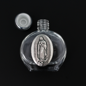 Glass holy water bottle with a metal embossed plaque of Our Lady of Guadalupe on the front. Plastic screw on cap that is a shiny silver tone color