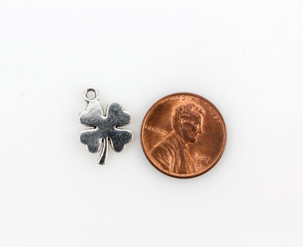 silver tone four leaf clover charm next to penny for size comparison