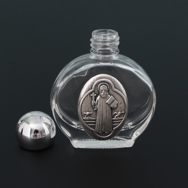 Glass holy water bottle with a metal embossed plaque of Saint Benedict on the front. Plastic screw on cap that is a shiny silver tone color.