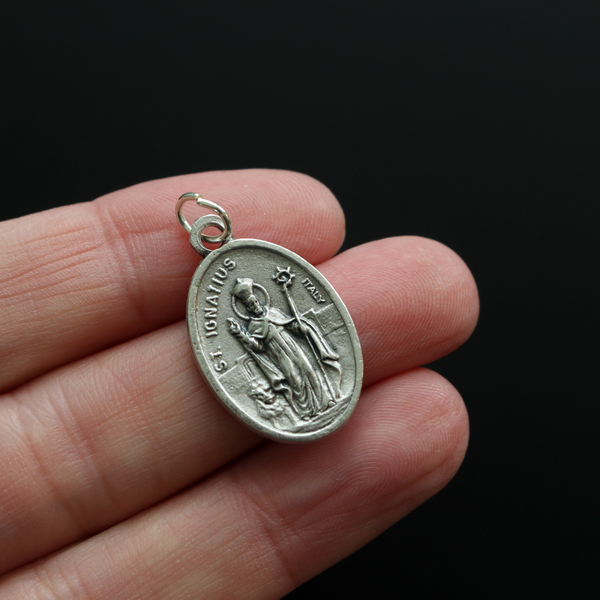 Saint Ignatius of Antioch medal that depicts the saint before a book and cross on the front and "Pray For Us" on the back