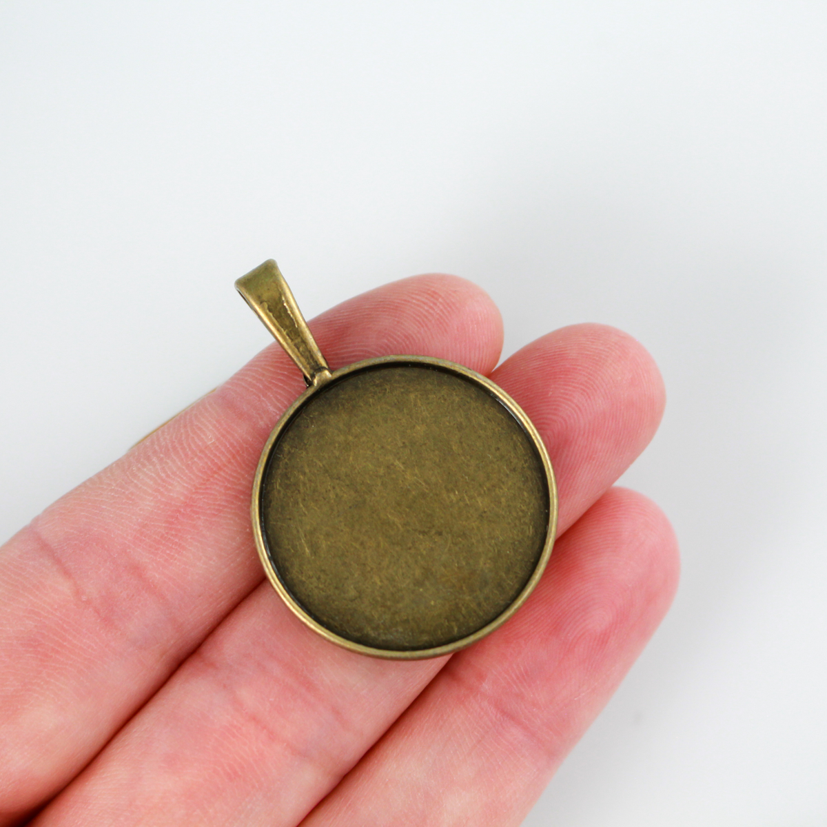 Round pendant cabochon setting in an antiqued bronze color. This is a flat edge bezel cup with a large bail loop. The tray fits 25mm cabochons