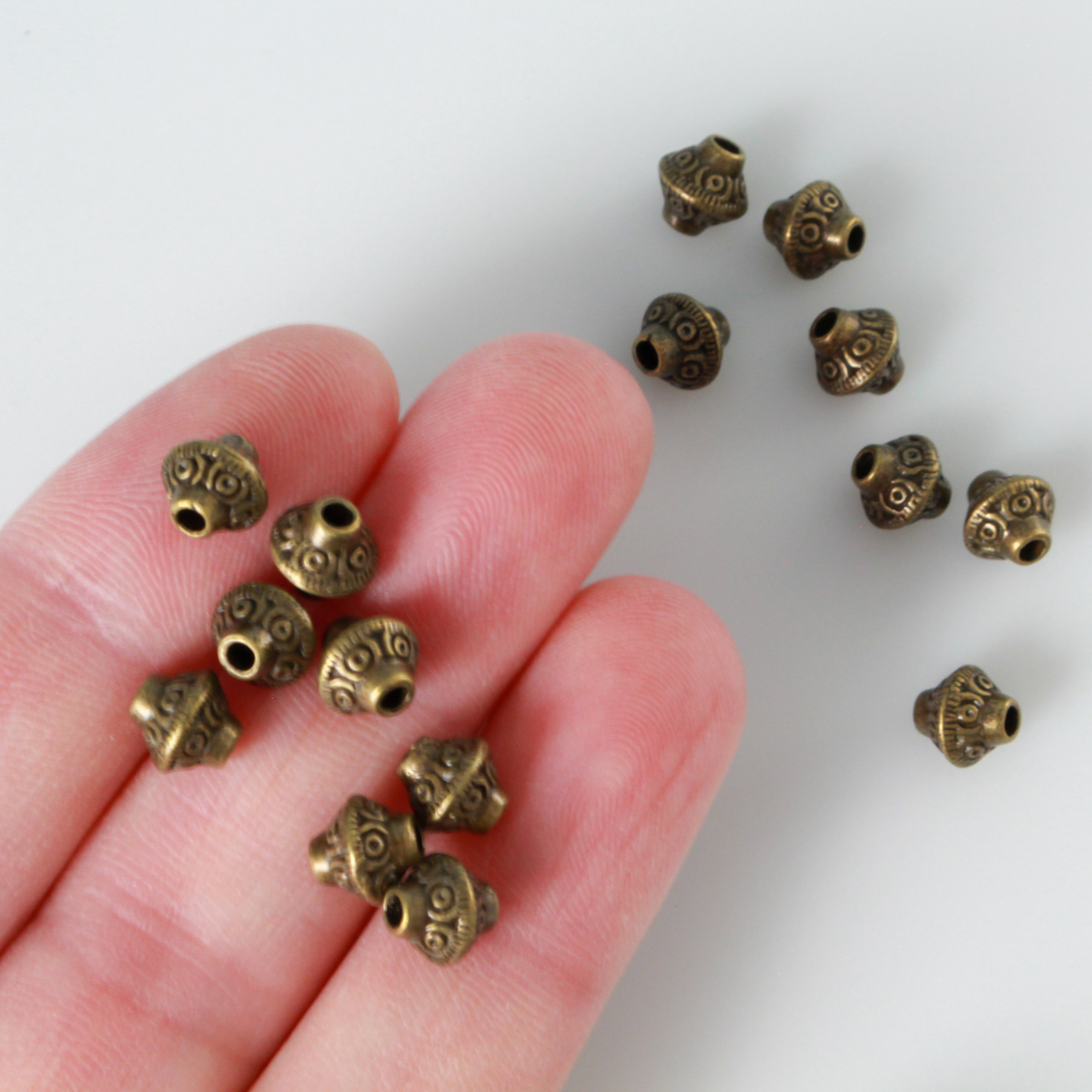 50 metal bicone shaped spacer beads with an antiqued bronze finish and a swirl pattern, 6mm x 6mm
