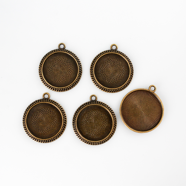 Round pendant cabochon setting in an antiqued bronze color. There is a pattern along the edge of the cup. The tray fits 25mm cabochons