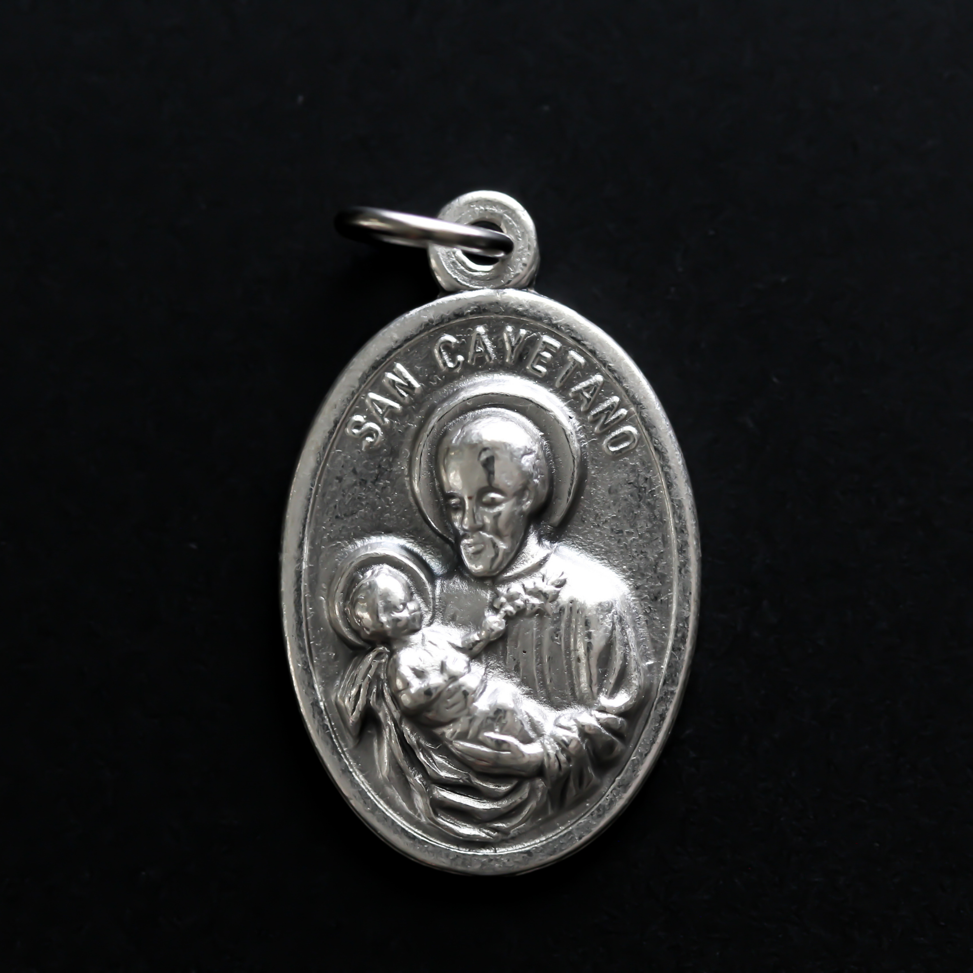 St. Cajetan (Cayetano) oval medal that depicts the saint on the front and "Pan Y Trabajo" on the back which translates from Spanish to "Bread and Labor"