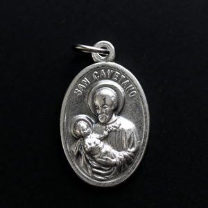 St. Cajetan (Cayetano) oval medal that depicts the saint on the front and "Pan Y Trabajo" on the back which translates from Spanish to "Bread and Labor"