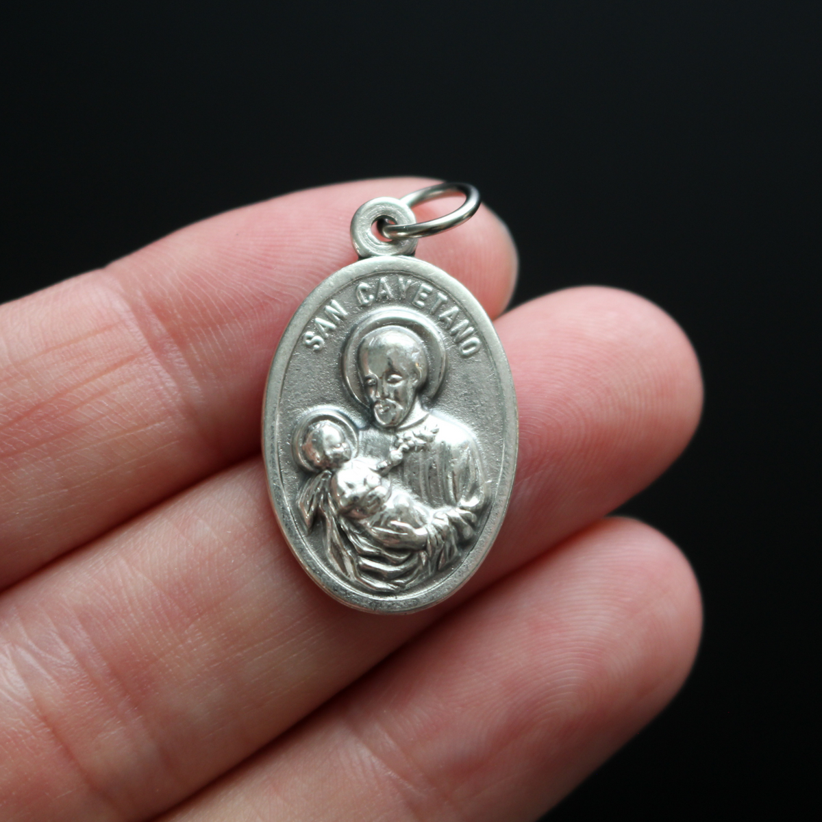 St. Cajetan (Cayetano) oval medal that depicts the saint on the front and "Pan Y Trabajo" on the back which translates from Spanish to "Bread and Labor"