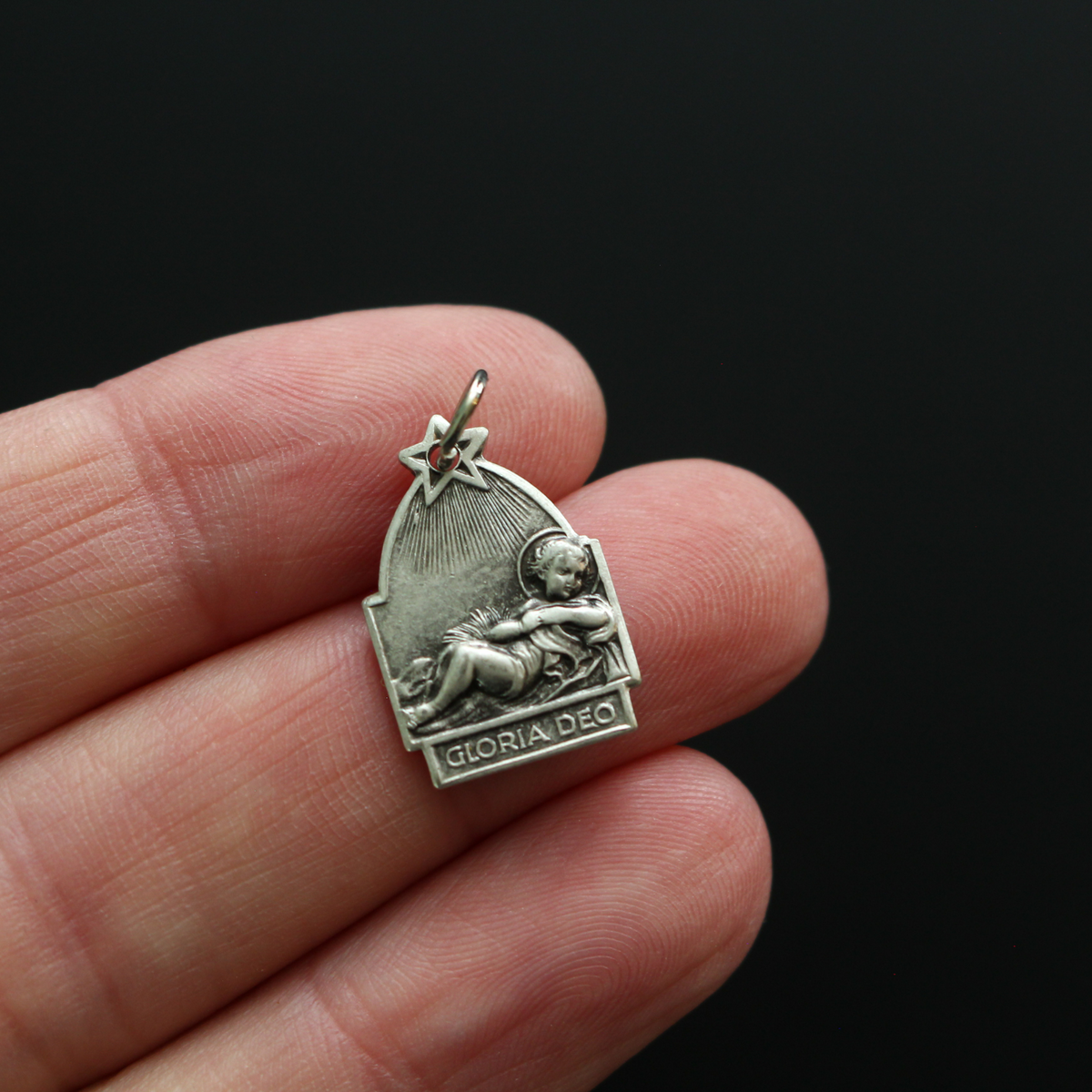 Antique reproduction nativity charm that depicts Jesus in the manger, the bail that holds the jump ring is star-shaped to represent the Star of Bethlehem